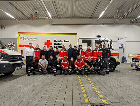 zu sehen ist ein Gruppenbild mit 16 neu ausgebildeten Sanitätshelfern und den Ausbildern vor einem DRK Fahrzeug
