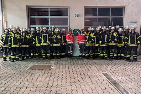 zu sehen ist ein Gruppenbild von Feuerwehr und DRK vor dem neuen Defi-Standort am Feuerwehr Gerätehaus in Weilheim
